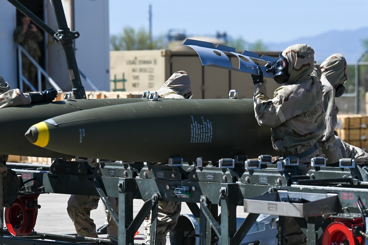 A person in hazardous material protective gear assembles a large bomb.