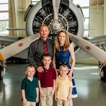 Man, woman, and three young boys stand in front of airplane