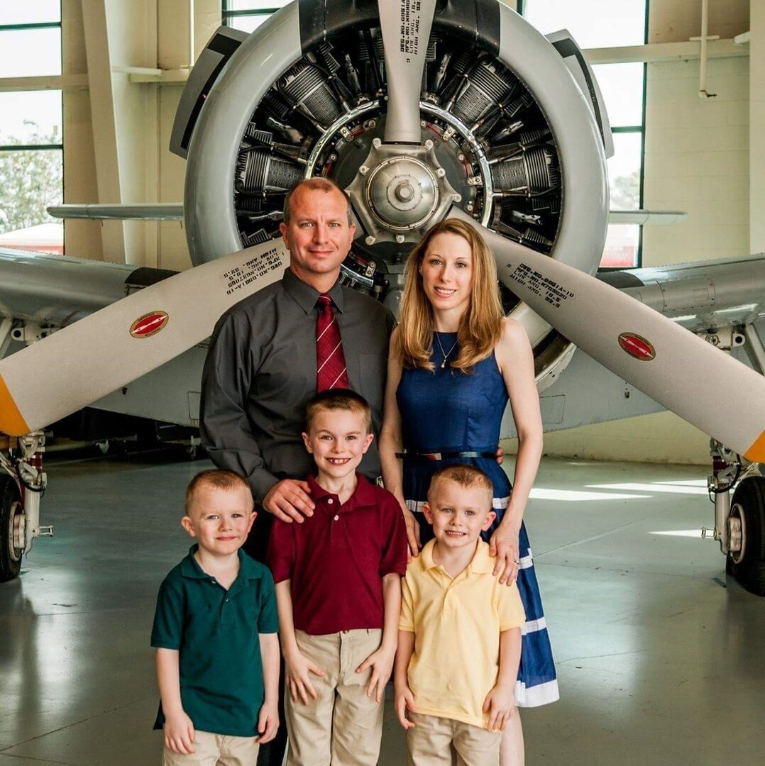Man, woman, and three young boys stand in front of airplane