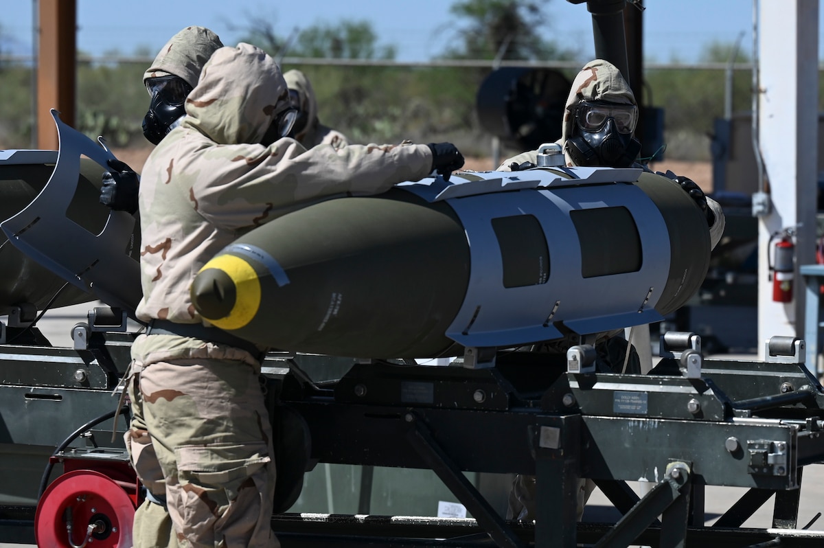 A photo of two people wearing military hazardous material protective gear assembling a bomb.