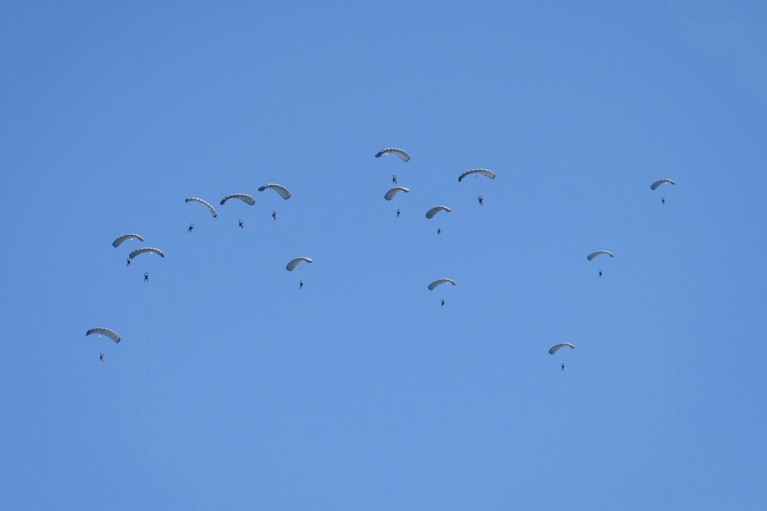 Airmen free-fall with parachutes in a blue sky.