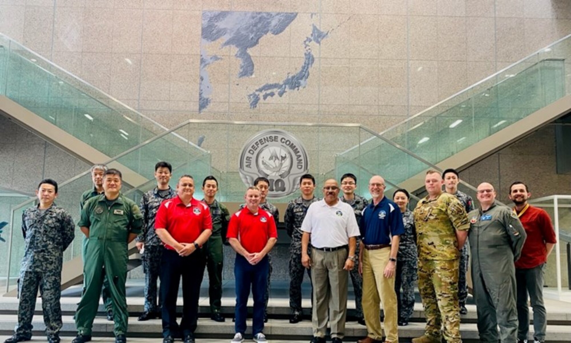 photo of uniformed U.S. Air Force Airmen and Japan air force members, and U.S. Air Force civilians standing in front of glass staircase.