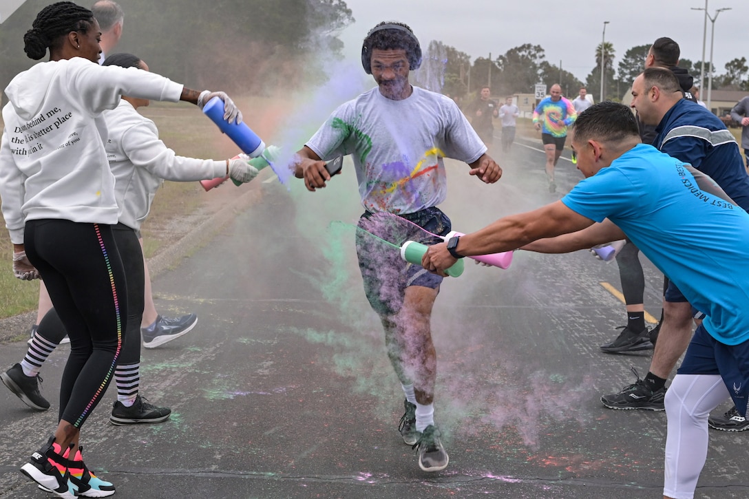 A service member is sprayed with colorful liquids as he runs down a road.