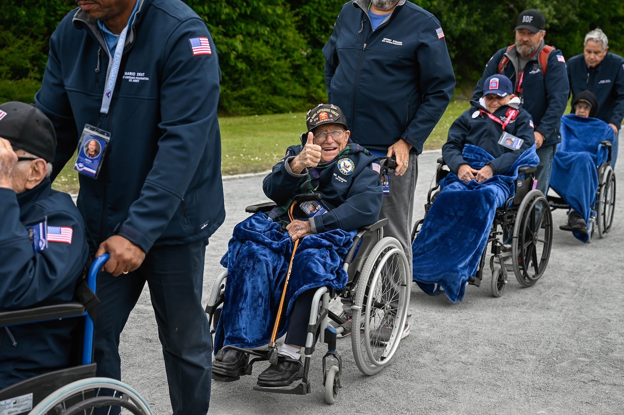 WWII veterans arrive in wheelchairs for a D-Day ceremony.