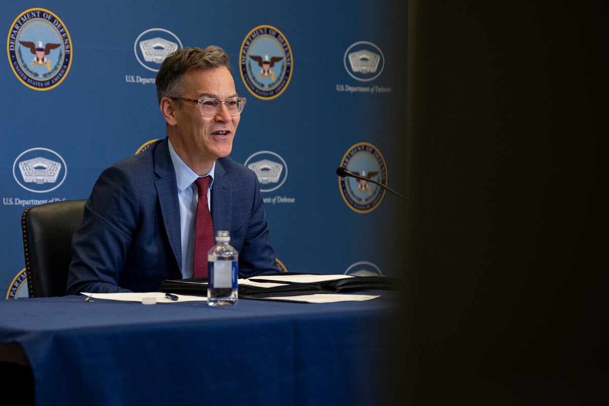 A man in suit is seated behind a microphone.