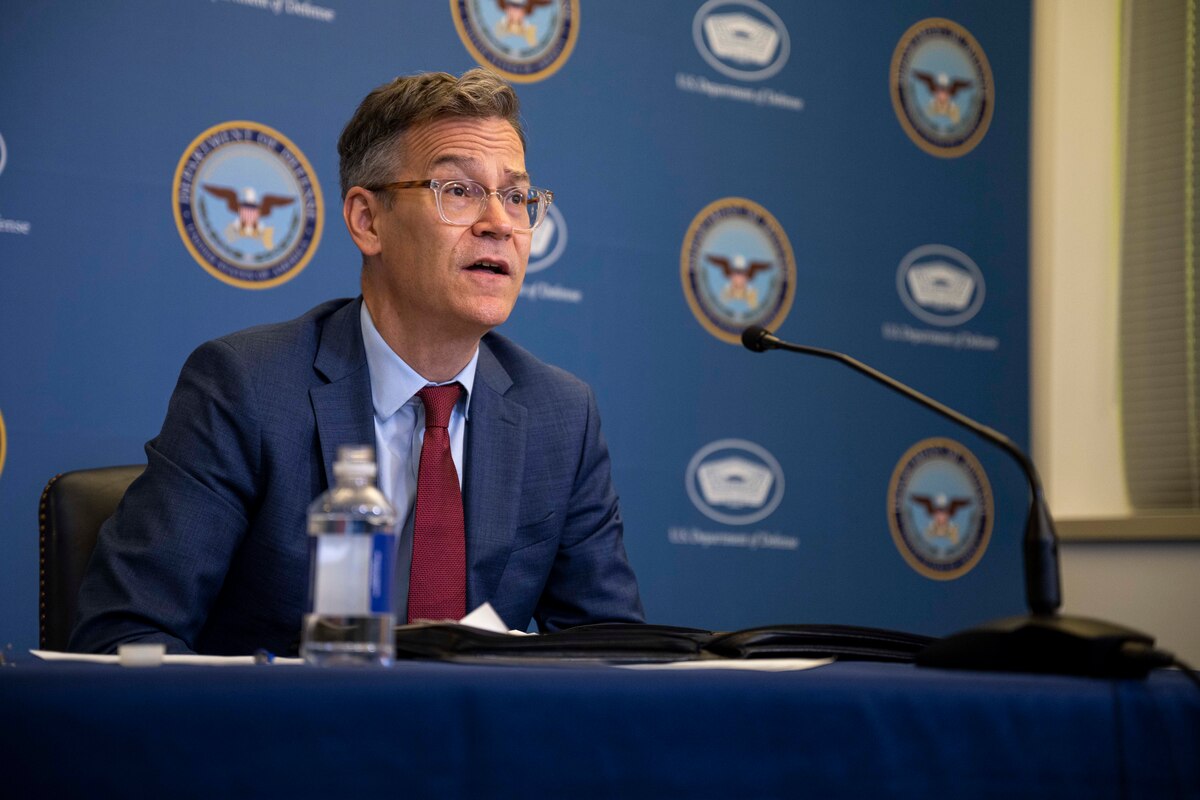 A man in suit is seated behind a microphone.