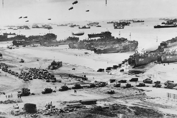 Ships and military personnel land on a beach in a black and white photo.