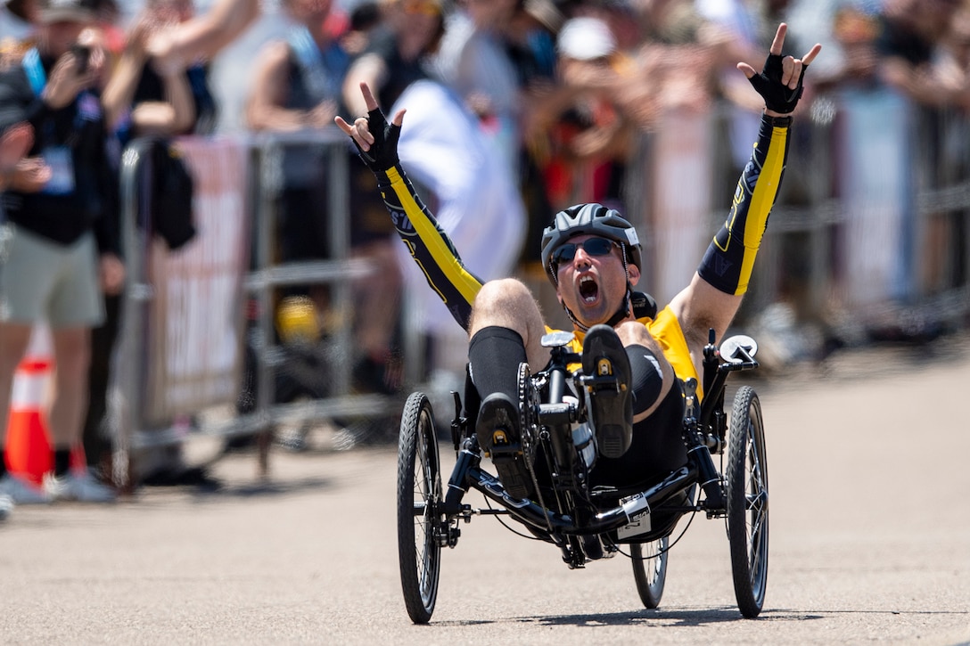 A race participant cheers while seated in a recumbent bicycle.