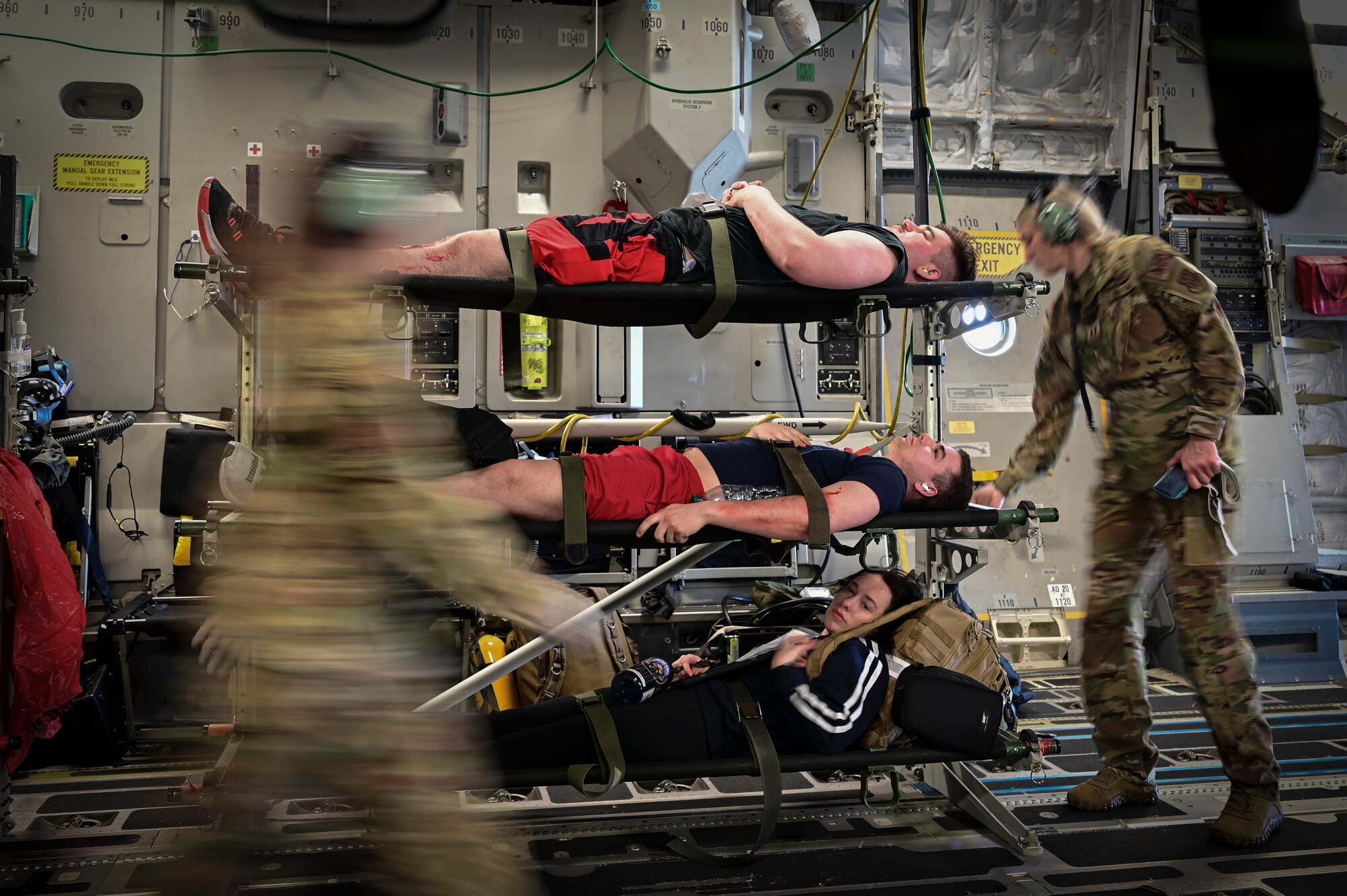 Amongst the business of a medical flight, three volunteer practice patients lay on stretchers stacked on top of each other like bunk beds as a medical tech adjusts the knob on the middle stretcher.