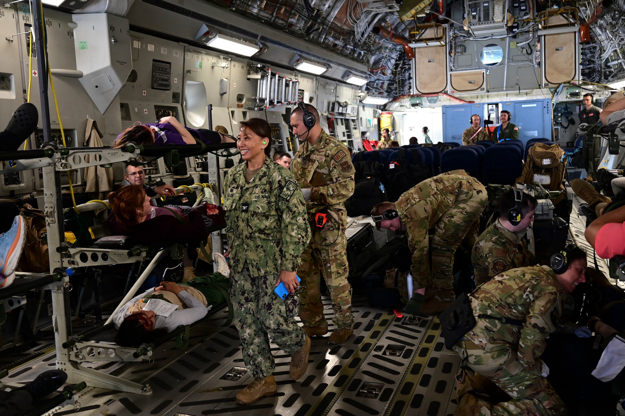 U.S. Airmen and Sailors work throughout a crowded C-17 Globemaster III that has been transformed into a flying ambulance full of various medical equipment and stretchers are stacked along the side of the interior of the aircraft.