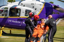 Dr. Andy Celestia, a flight physician, Nicole Hardie, a flight nurse, and a LifeFlight pilot strap a Sailor assigned to Naval Air Station Whidbey Island Search and Rescue to a stretcher at Naval Station Everett (NSE), June 6, 2023. NSE participated in a regional aircraft emergency response training exercise that includes aircraft and first responders from state, county, and local partner agencies in the Northwest Regional Aviation consortium. The training focuses on preparing for a potential real-world earthquake and tsunami disaster response. The exercise will help participating organizations, including the Navy, improve their ability to work together to support local emergency responders in a large-scale organized response. (U.S. Navy photo by Mass Communication Specialist 2nd Class Ethan Soto)