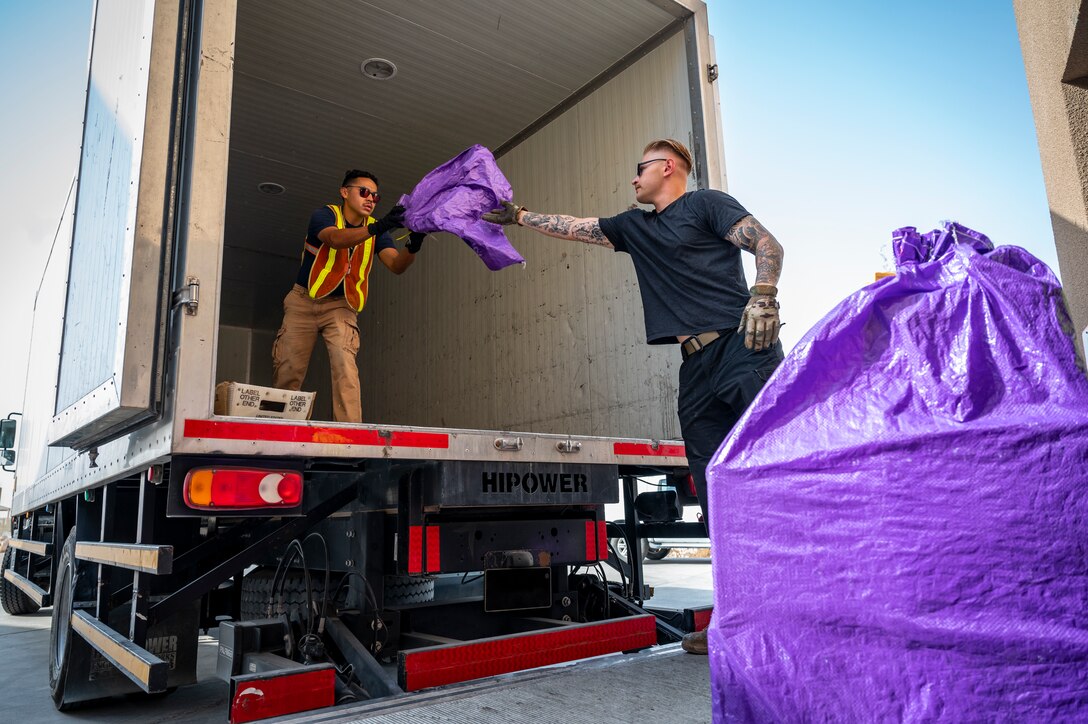 Two military members pass mail to each other on a truck to load.