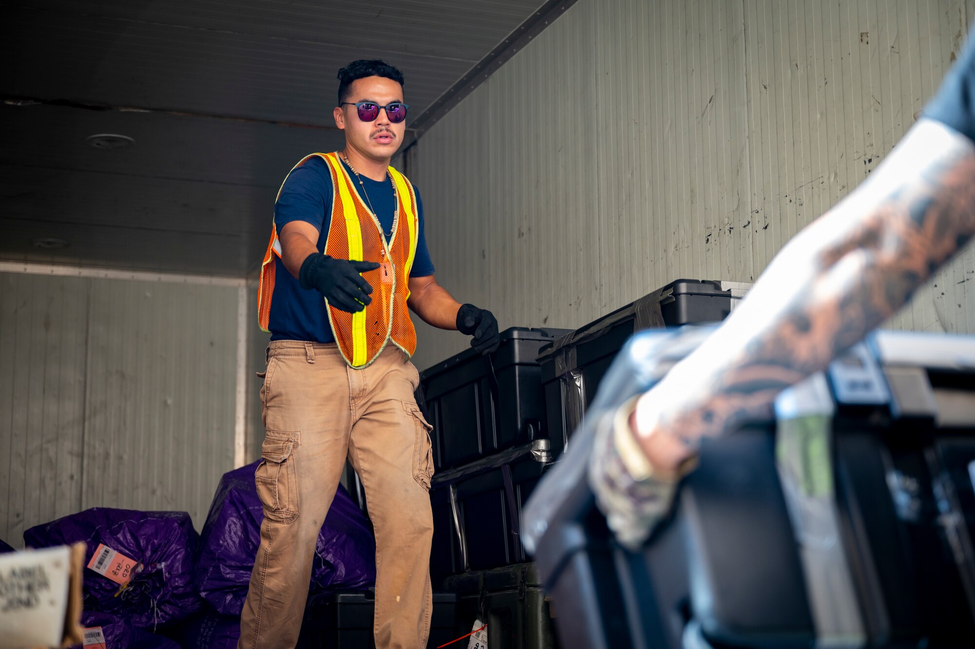 A military member in the back of a truck reaches out to grab a package.