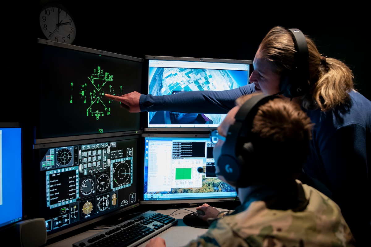 Air Force Research Laboratory, or AFRL, Controls Engineer Capt. Christian Potts, left, and Program Manager Amy Burns, right, watch from the simulation control room at AFRL’s Aerospace Systems Directorate while 2nd Lt. Ryan Collins demonstrates automatic fly up maneuvers in a virtual flight simulator generated by the Automatic Ground Collision Avoidance System, or Auto GCAS, Dec. 6, 2022, at Wright-Patterson Air Force Base, Ohio. Auto GCAS is a software update developed by AFRL, Lockheed Martin and NASA that prevents an aircraft from impacting the ground by automatically pulling the aircraft up before an accident can occur. Kerianne Hobbs, safe autonomy and space lead with the Autonomy Capability Team, or ACT3, for the Sensors Directorate at AFRL, was the lead author of a 38-page spread in the Institute of Electrical and Electronics Engineers Control Systems Magazine, titled Runtime assurance for safety-critical systems: An introduction to safety filtering approaches for complex control systems, for her extensive research in runtime assurance. (U.S. Air Force photo / Richard Eldridge)
