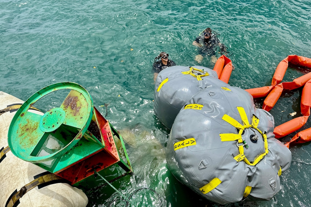Divers float in the water near a large buoy.