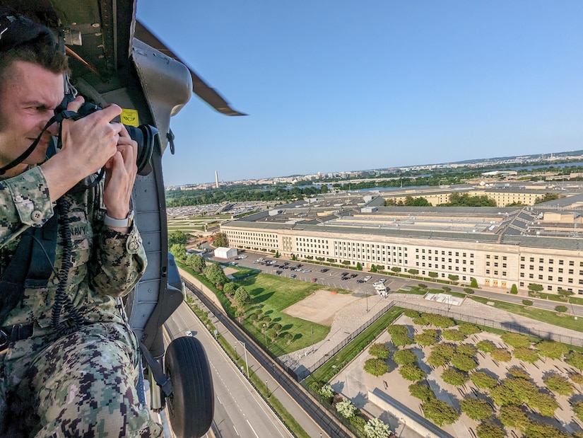 A man points a camera outside of the open door of a helicopter as it flies over the Pentagon.