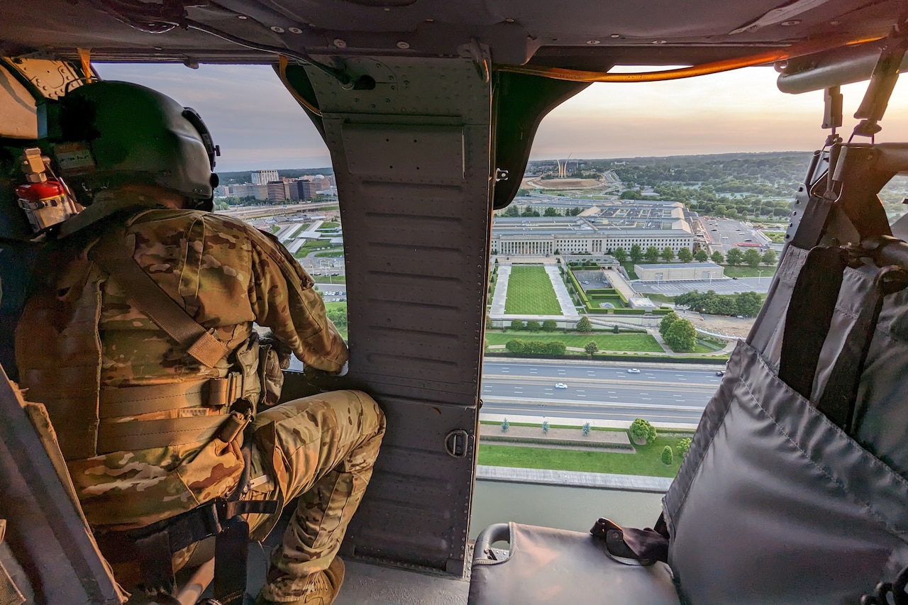 A man looks out of an open window inside a helicopter as it flies over the Pentagon.