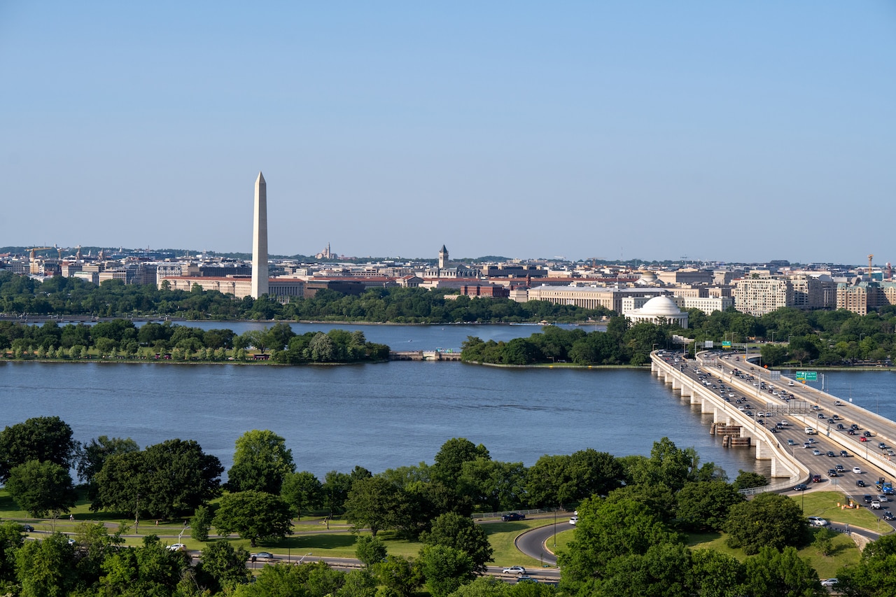 An aerial view of a bridge crossing a river. In the background is the Washington Monument.