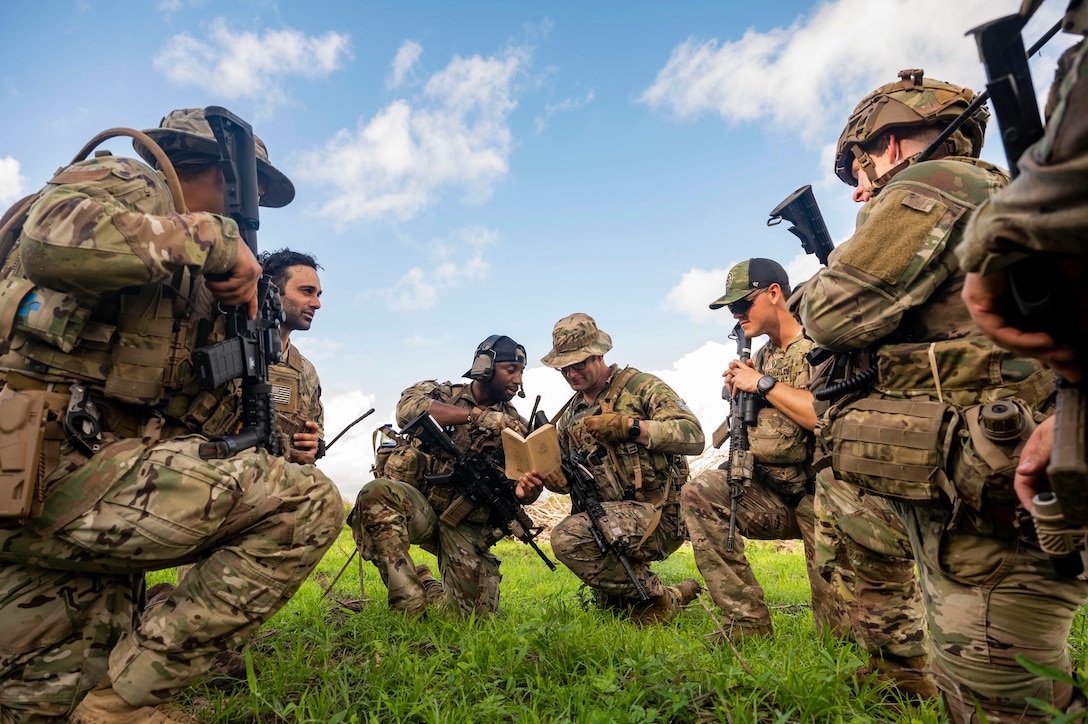 Two groups service members kneel facing each other while two look at a notebook together.