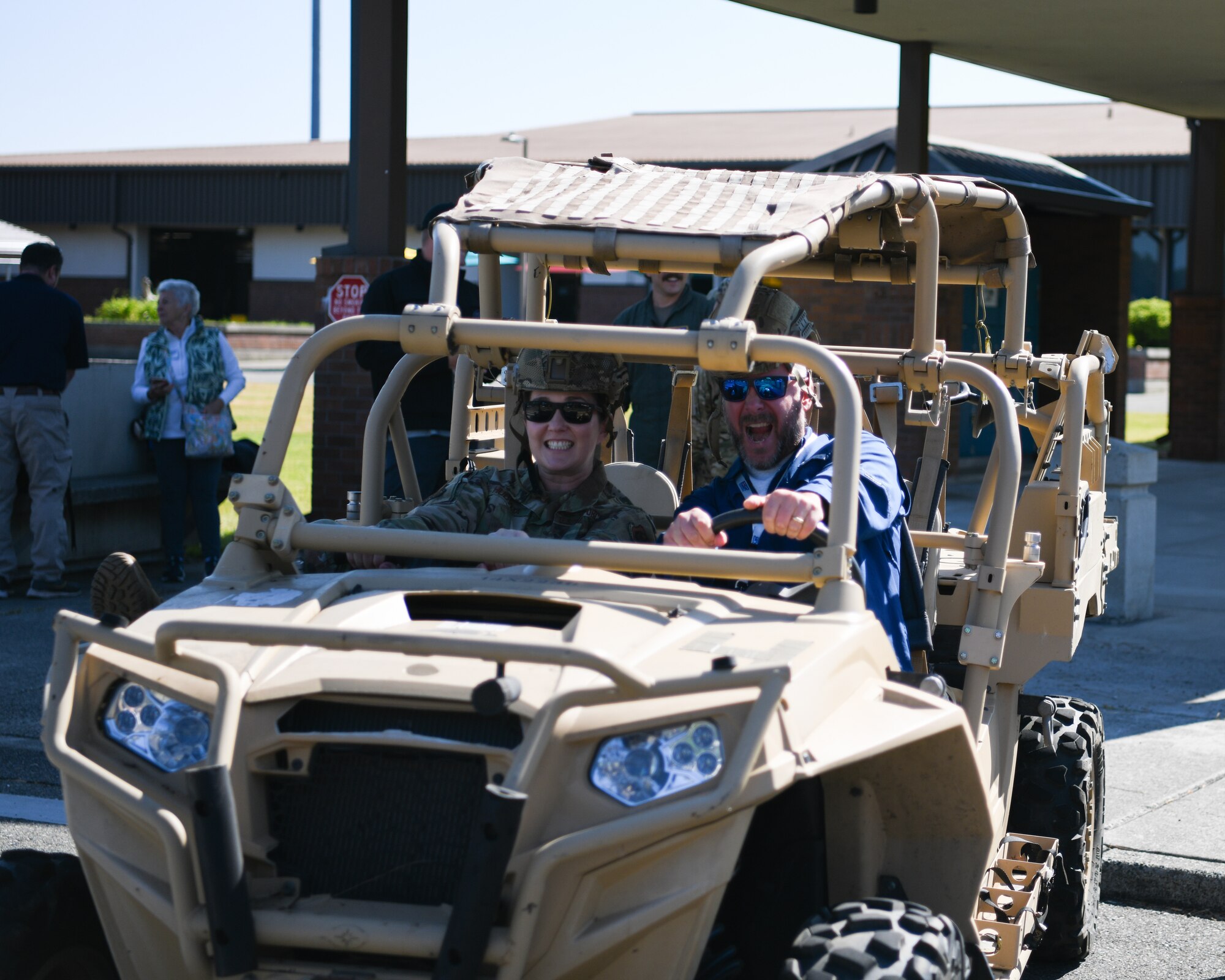 An airman sits in an open ATV like vehicle that is tan with a civilian employer as they pose for a photo.