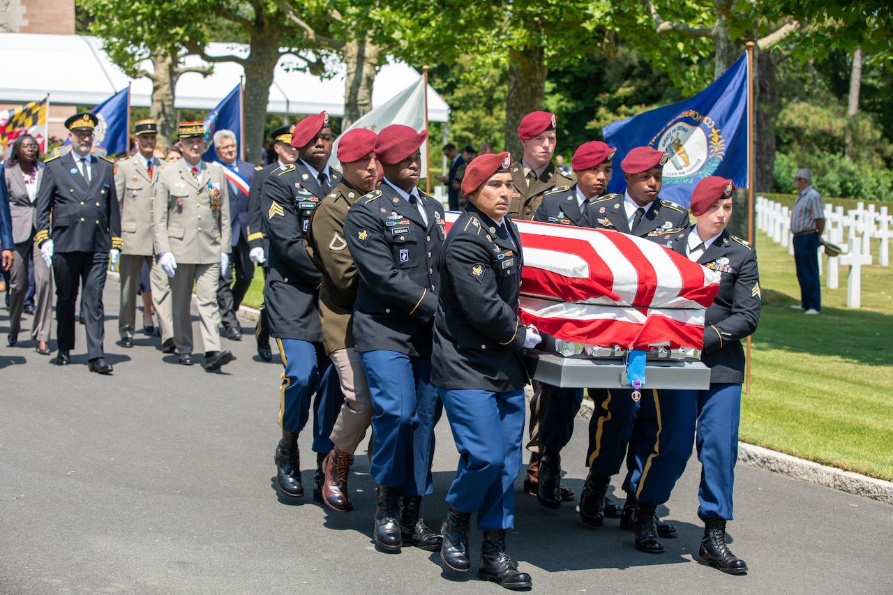 Service members in uniform carry a casket draped by a U.S. flag.