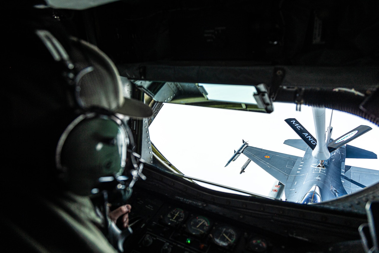 An airman watches a jet receive fuel outside the window of a refueler.
