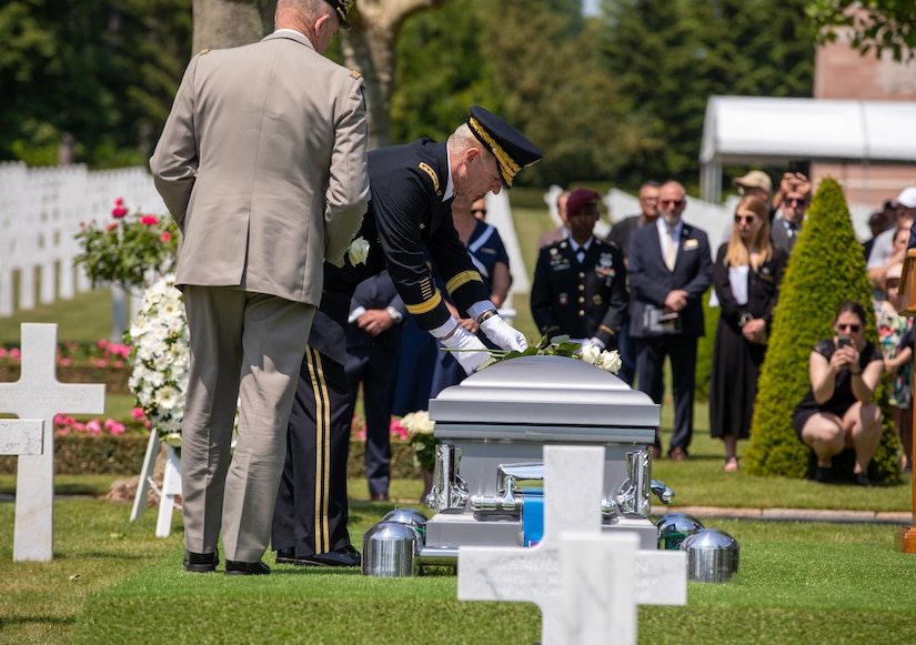 A man in uniform places a flower on a coffin.