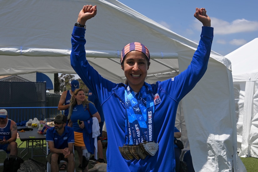 An airman raises her hands while wearing five medals around her neck.