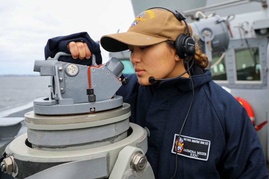 A sailor looks through equipment to survey the horizon.