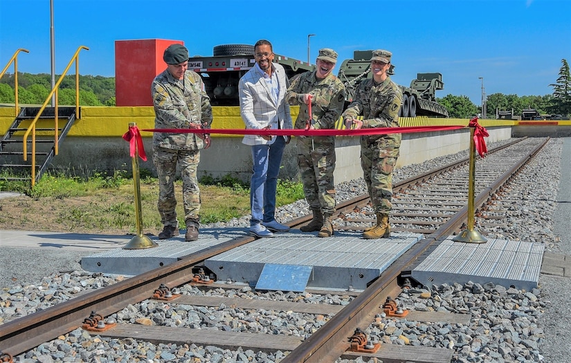 Leadership from U.S. Army Garrison Benelux and local mission partners prepare to cut a ribbon during a ceremony marking the reopening of the rail line at Eygelshoven Army Depot, the Netherlands, May 19, 2023. During the ceremony, speakers highlighted the additional logistics capabilities and strategic flexibility available with the addition of a functional rail line at the site. (U.S. Army photo by Meredith Mulvihill, USAG Benelux Public Affairs)