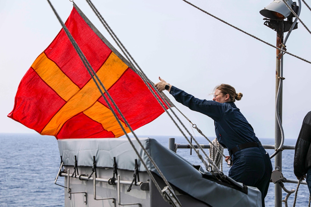 A sailor brings down a flag on the deck of a ship.