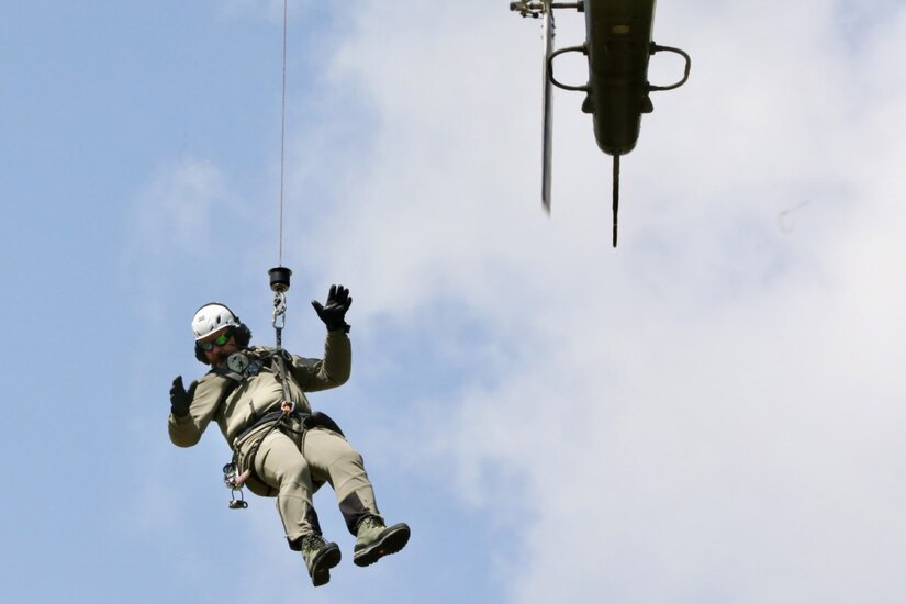 A soldier is hoisted to an airborne helicopter.