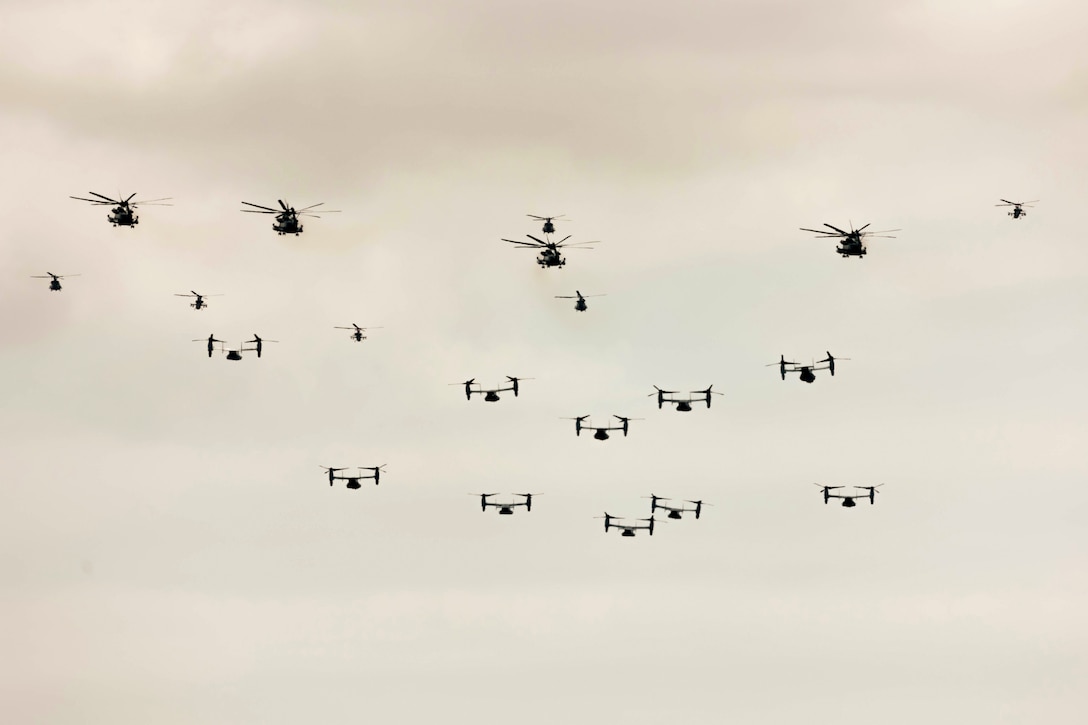 A large group of Marine Corps aircraft fly together in a hazy sky.