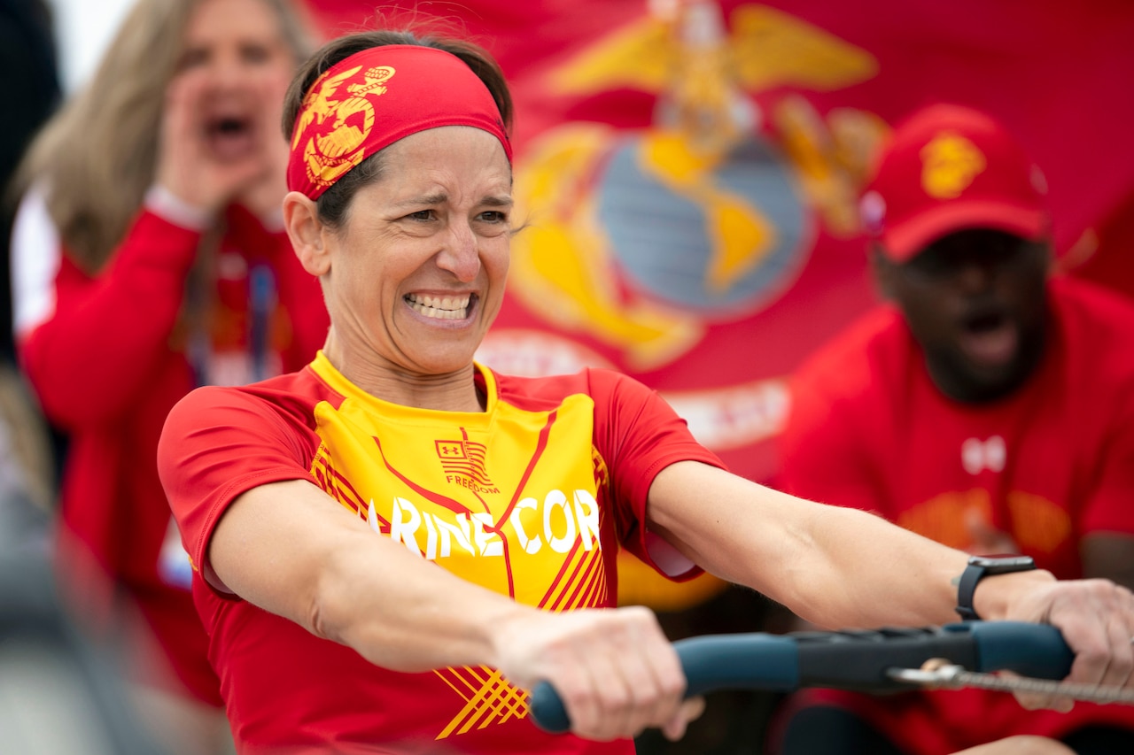 A Marine pulls a rowing machine as blurred spectators cheer in the background.