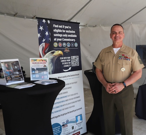 A marine stands next to a recruiting stand.