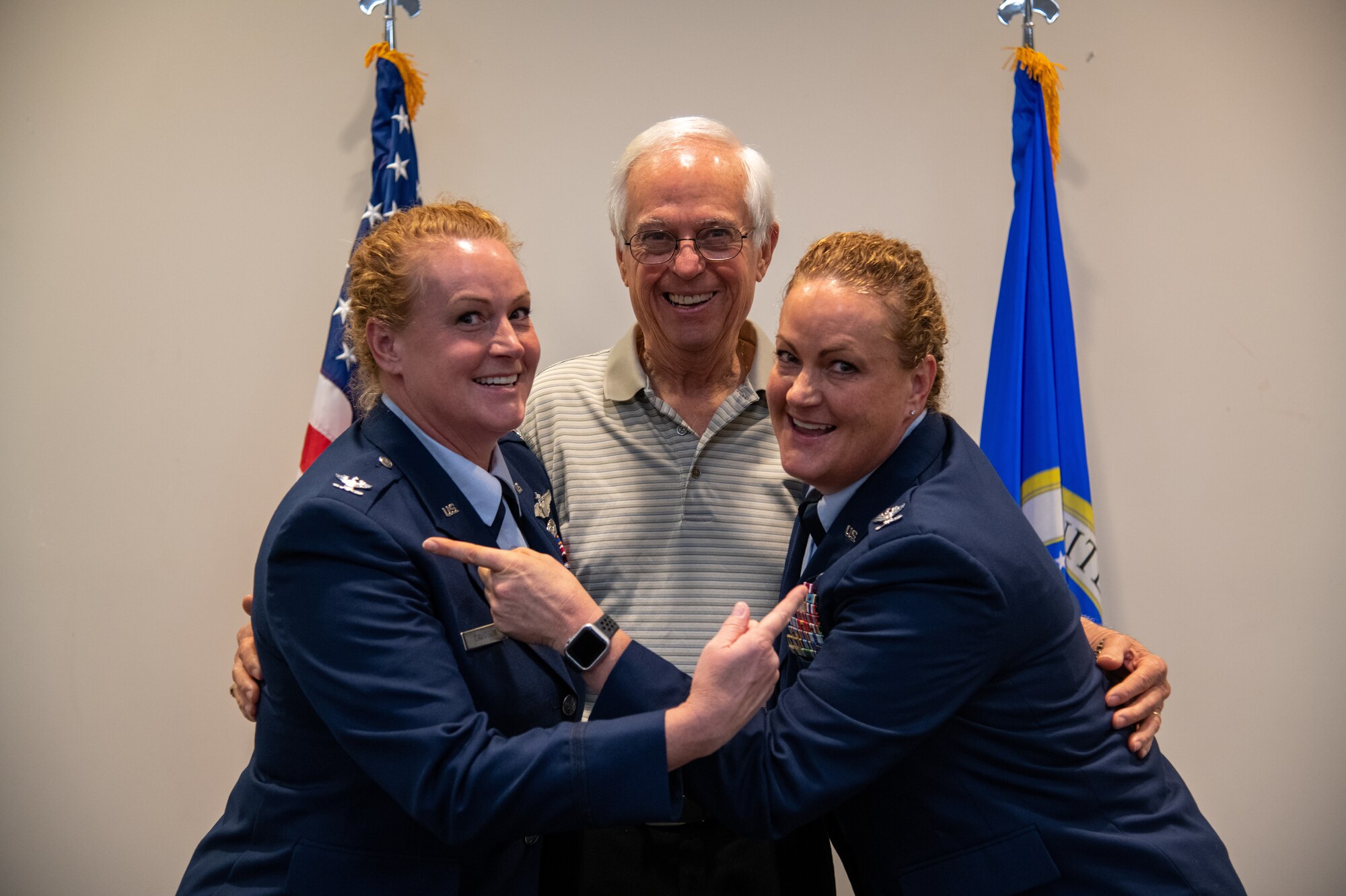 Two twin sisters in military uniform point at their same ranks with their father in the middle in civilian clothes.