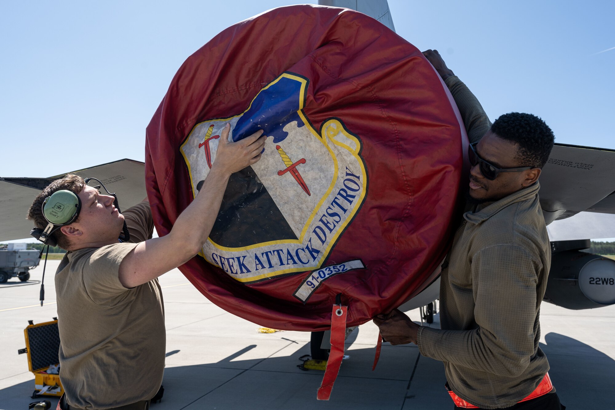 U.S. Air Force Staff Sgt. Zane House, 480th Fighter Generation Squadron crew chief, left, and Senior Airman Samuel Brown, 480th FGS crew chief, put an exhaust cover on an F-16 Fighting Falcon at Powidz Air Base, Poland