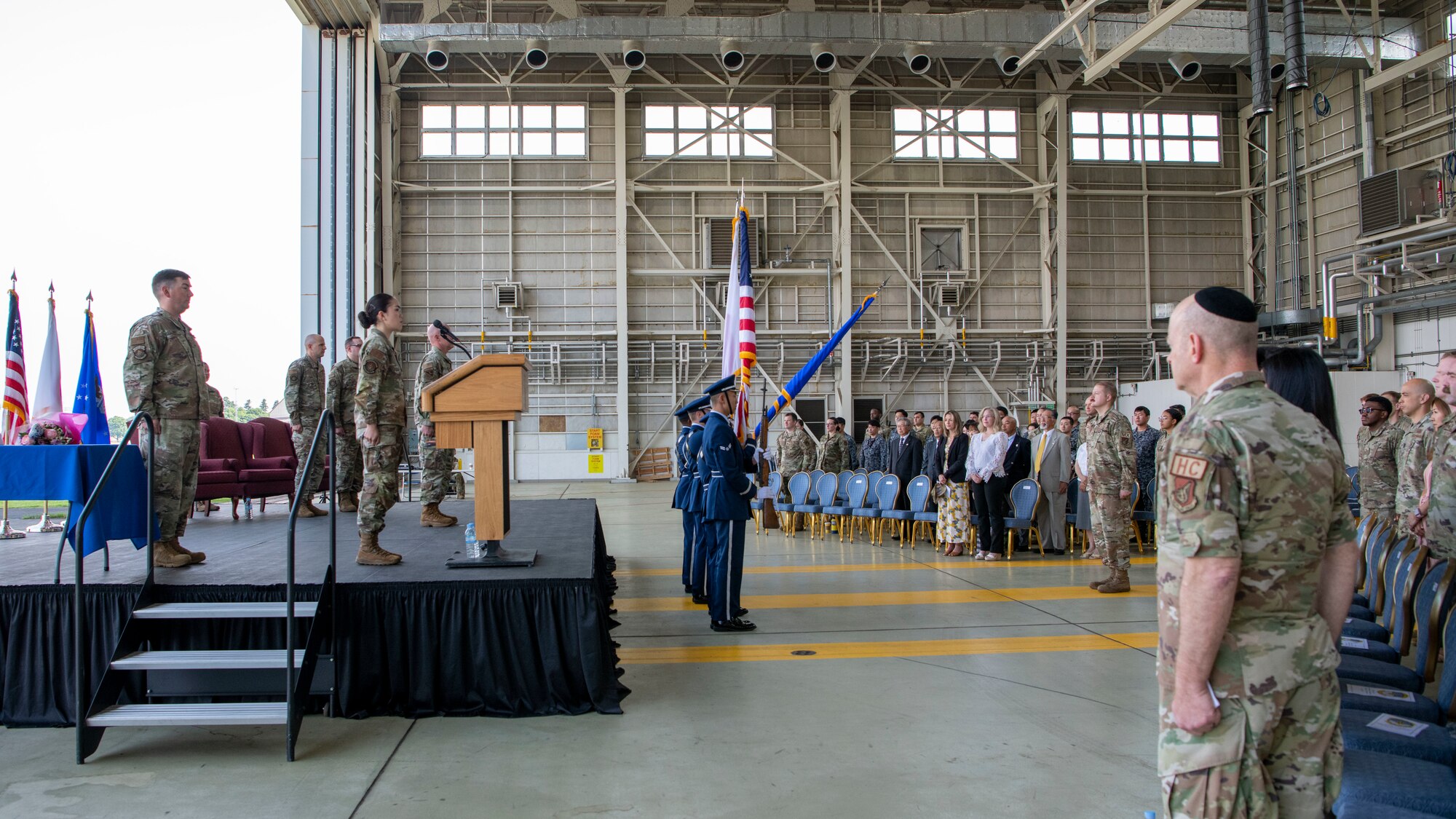 A large crowd faces a stage standing stiffly for a playing of the National Anthem
