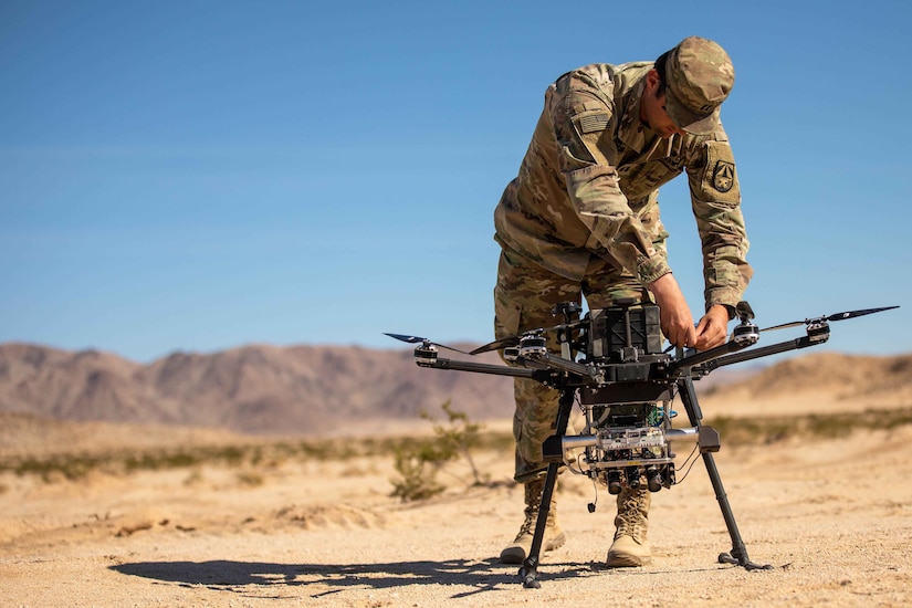 A soldier in uniform handles a small quadcopter drone.