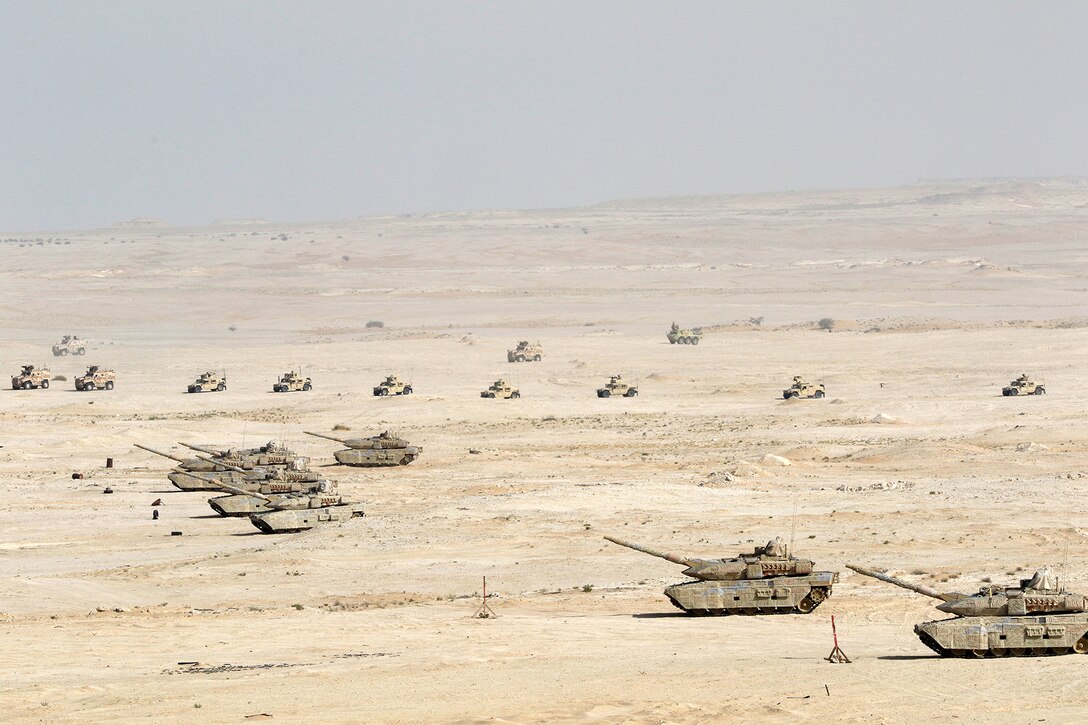 Military tanks and vehicles cross the desert.