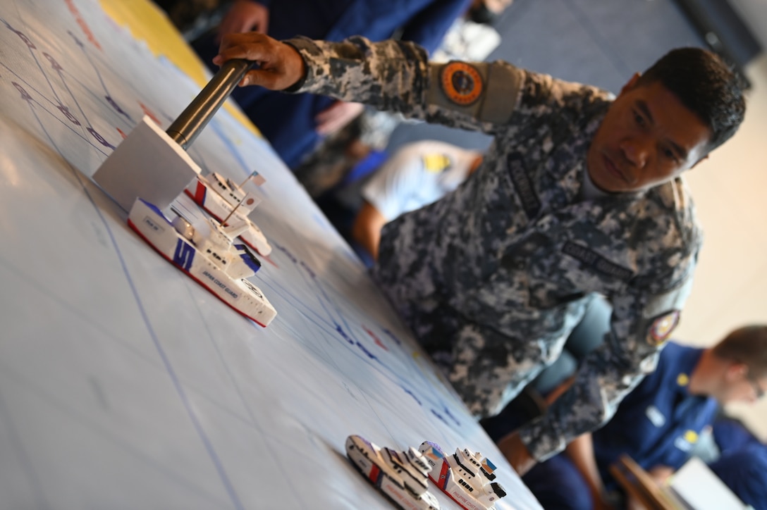 A Philippine Coast Guard service member positions a model ship during a collaborative mission planning meeting with members from the U.S. Coast Guard Cutter Stratton (WMSL 752), the Japan Coast Guard Vessel Akitsushima (PLH 32) and the Philippine Coast Guard, before departing Manila, Philippines, to conduct joint at-sea operations, June 3, 2023. Stratton deployed to the Western Pacific to engage with regional allies and partner nations, reinforcing a rules-based order and maritime governance to promote a free and open Indo-Pacific. (U.S. Coast Guard photo by Chief Petty Officer Matt Masaschi)