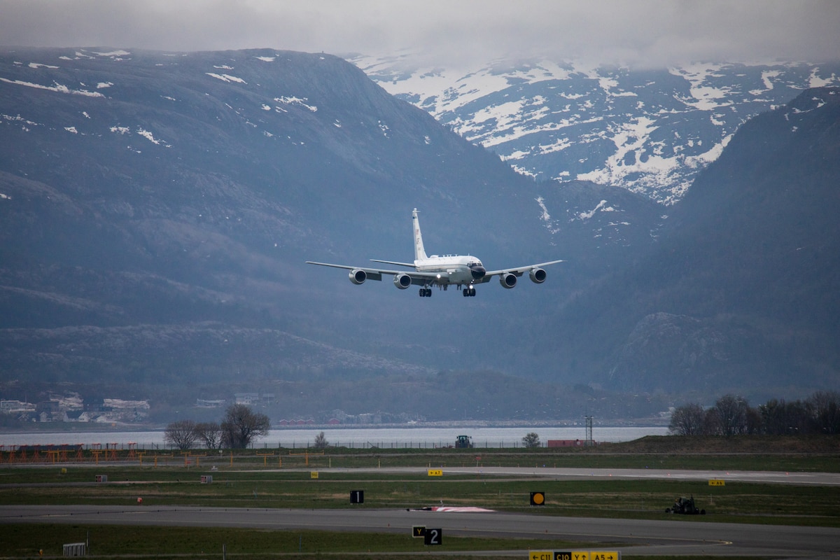 An aircraft comes in for a landing with a backdrop of snow-topped mountains