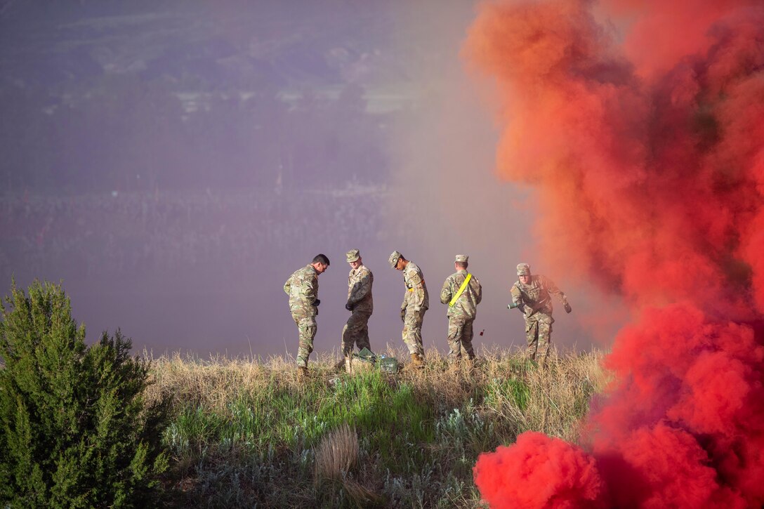 Five soldiers stand in a grassy area with thick red-orange smoke to the right.