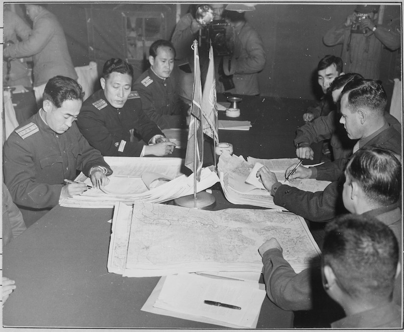 Men seated at a table look at documents.
