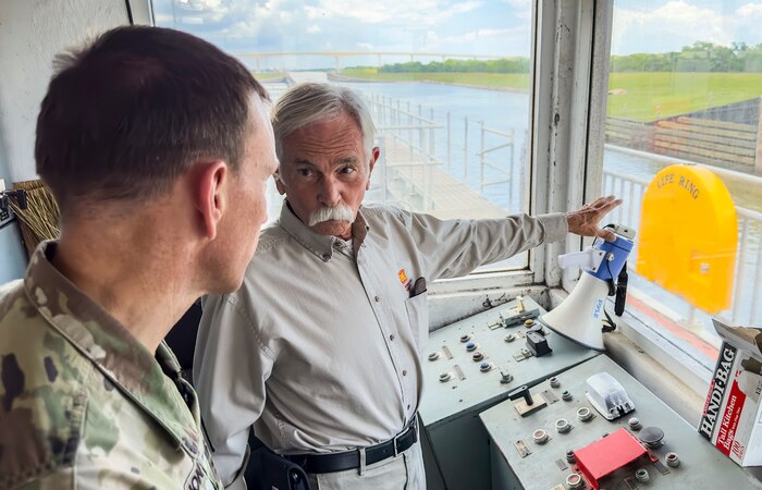 two men are standing in a booth talking while one man is pointing out a window