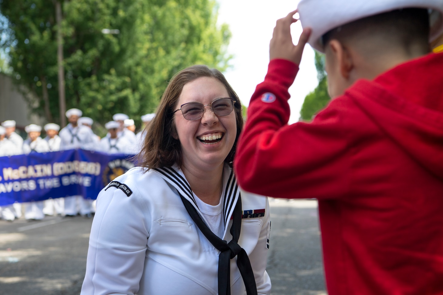 Logistics Specialist 2nd Class Autumn Hoadley, assigned to USS Kansas City (LCS 22), shares her cover with a child at the annual Rose Festival Parade during Portland Fleet Week in Portland, Oregon, June 10, 2023. Portland Fleet Week is a time-honored celebration of the sea services and provides an opportunity for the citizens of Oregon to meet Sailors, Marines and Coast Guardsmen, as well as witness firsthand the latest capabilities of today's maritime services. (U.S. Navy photo by Mass Communication Specialist Seaman Sophia H. Bumps)