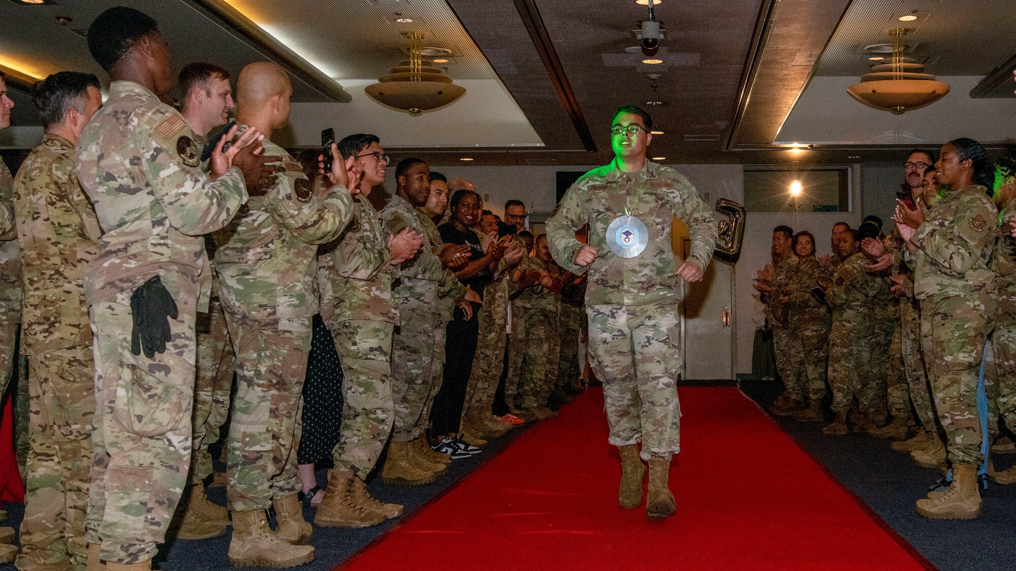 A soldier struts down an aisle with crowds of soldiers on either side cheering.