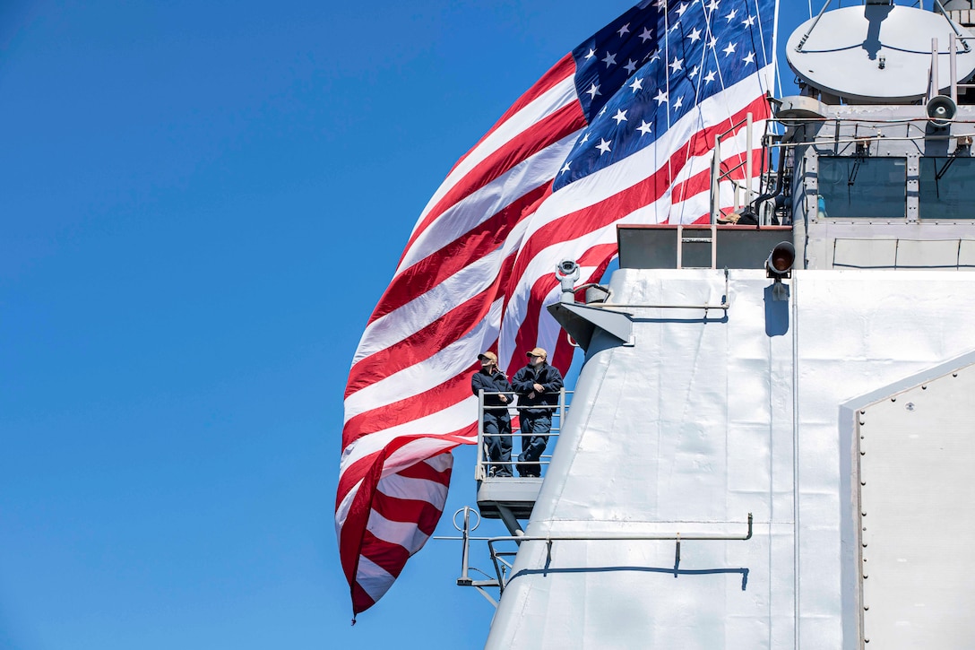 Two sailors observe from the side of a Navy ship.