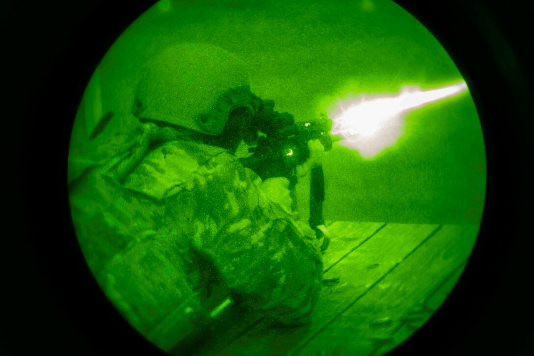 An airman illuminated by green light fires a weapon.