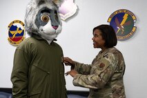 U.S. Air Force Chief Master Sgt. Adrienne Warren, 99th Air Base Wing (ABW) command chief, puts a 99th ABW patch on BUCKET$, the Las Vegas Aces mascot, at Nellis Air Force Base, Nevada, June 9, 2023.